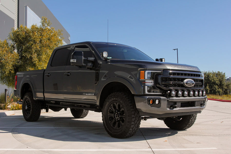 Bumper Light Kits by Baja Designs: A dark gray Ford Super Duty pickup in a parking lot with Squadron fog pocket lights in the bumper and extra LED pods on the grille and pillars.