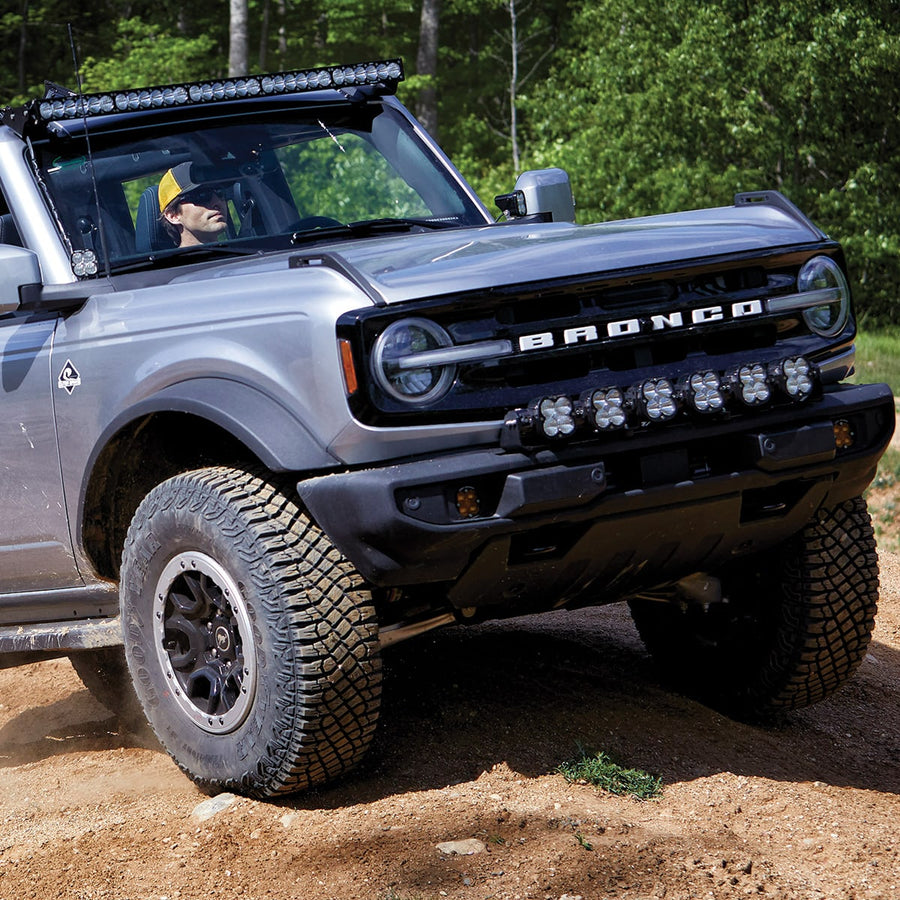 Bumper Light Kits by Baja Designs: Front corner of a silver Ford Bronco on a dirt trail with six linkable LED pods mounted across the front bumper.