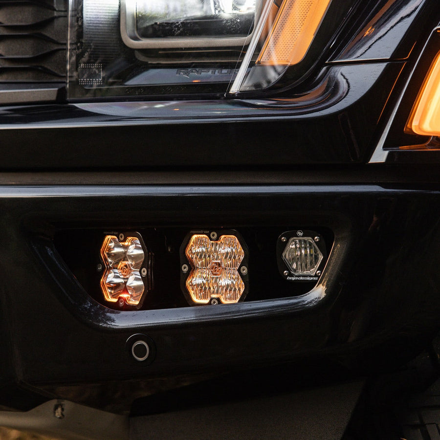Fog Light Kits by Baja Designs: Two square pods with amber backlights and a small S1 pod installed in the fog pocket of a black Ford Raptor.