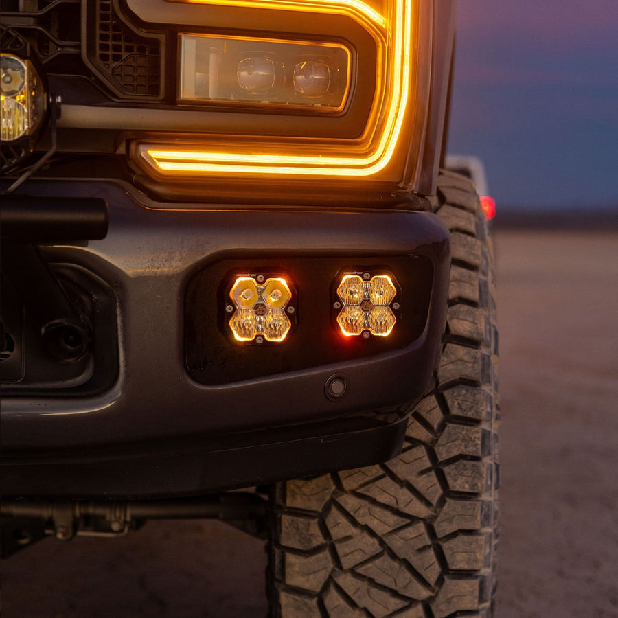 Fog Light Kits by Baja Designs: Two square pods with amber backlights glow in the lower bumper of a dark Ford Super Duty at dusk.