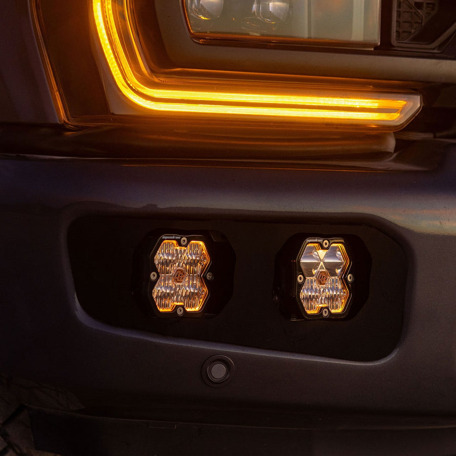 Fog Light Kits by Baja Designs: Two square pods with amber backlights installed in the twin fog pocket of a dark Ford Super Duty bumper.