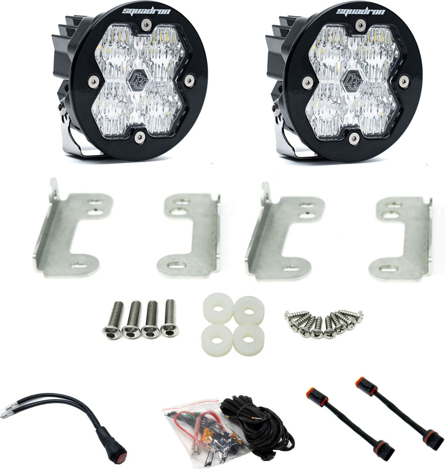 Fog Light Kits by Baja Designs: Pair of round Squadron-R pods with clear lenses, four stainless fog brackets, bolts, spacers, wiring harness and adapters on white.