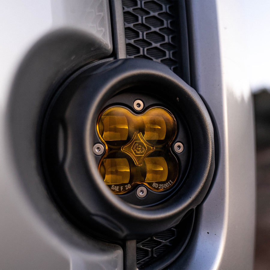 Fog Light Kits by Baja Designs: Close view of a round amber-lens fog pod mounted in a silver bumper fog pocket beside a black mesh grille.
