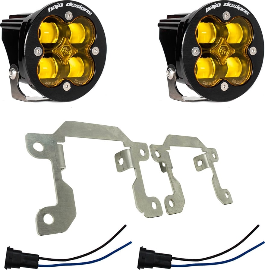 Fog Light Kits by Baja Designs: Two round black Squadron SAE fog pods with amber lenses, two silver mounting brackets and two pigtail harnesses on white.