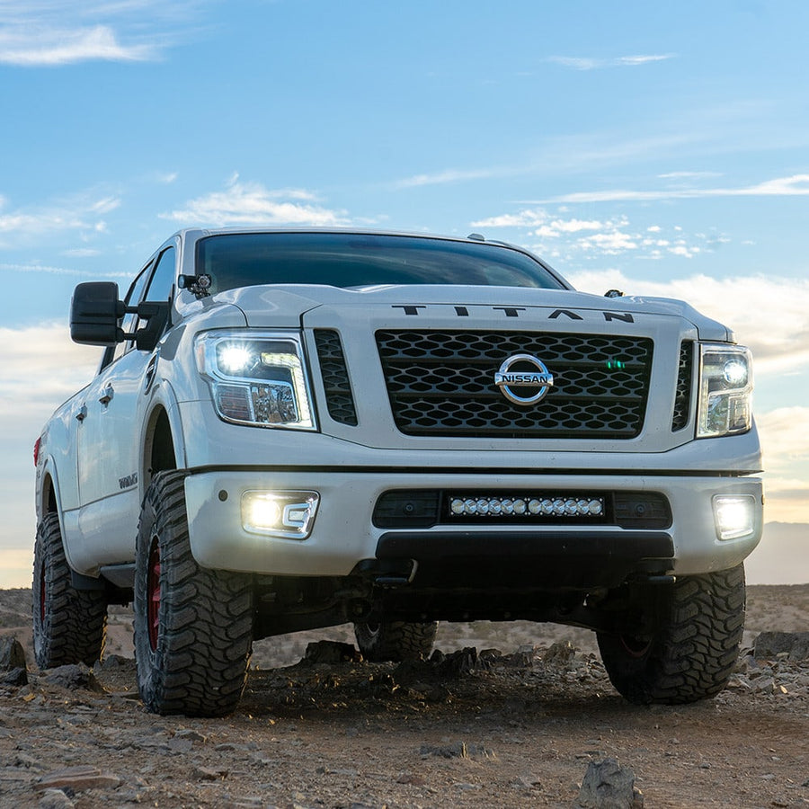 Fog Light Kits by Baja Designs: A white Nissan Titan XD on a rocky hillside with clear fog lights glowing beside a lower bumper light bar.