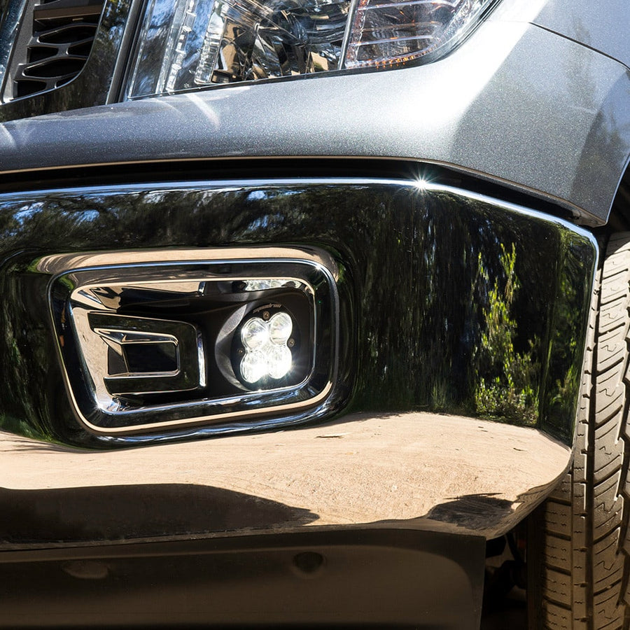 Fog Light Kits by Baja Designs: Close view of a clear Squadron fog light glowing inside a chrome fog pocket bezel on a gray vehicle.