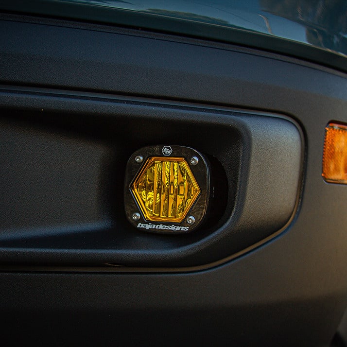 Fog Light Kits by Baja Designs: Close view of an amber S1 pod set in a black plastic fog pocket next to an amber side marker.