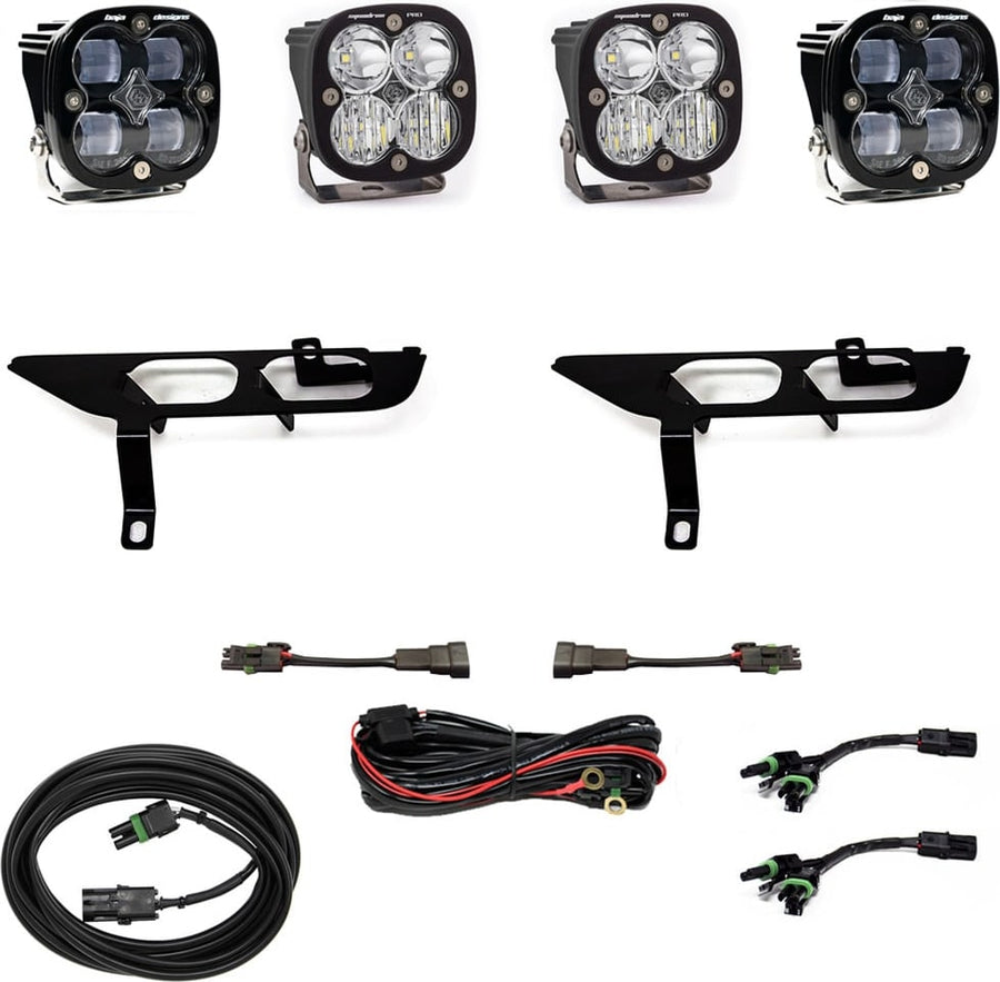 Fog Light Kits by Baja Designs: Four black Squadron pods with clear lenses, two black fog pocket brackets, a red relay harness, adapter harnesses and coiled cables on white.
