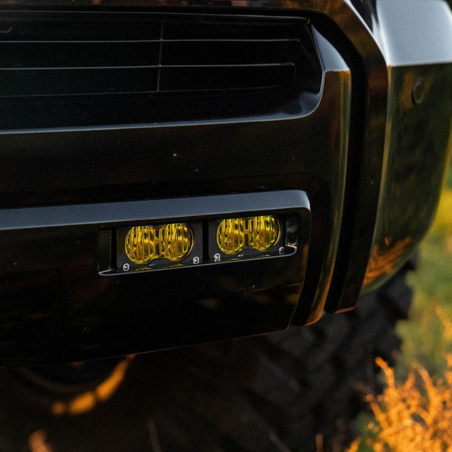 Fog Light Kits by Baja Designs: Two S2 pods with amber lenses mounted in the lower bumper fog opening of a dark SUV at golden hour.