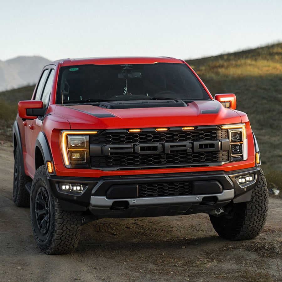 Fog Light Kits by Baja Designs: A red Ford Raptor on a dirt road with S2 fog pocket lights glowing in the lower bumper.