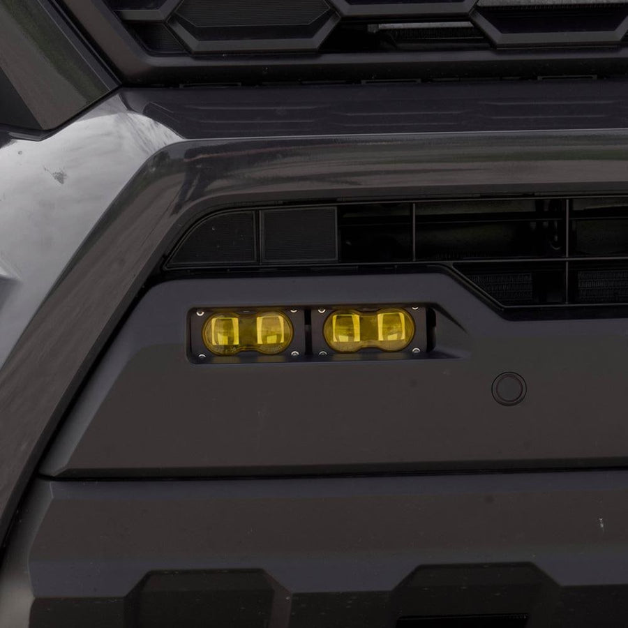 Fog Light Kits by Baja Designs: Close view of two amber S2 pods seated in a dark Toyota Tacoma lower fog pocket.