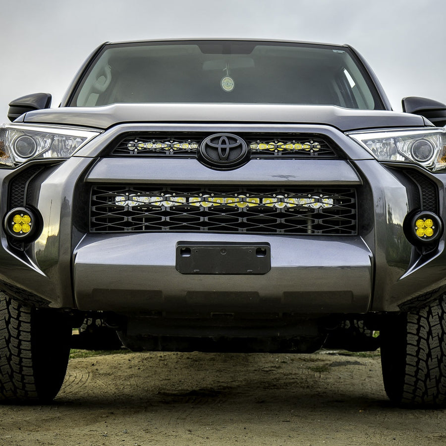 Grille Light Kits by Baja Designs: Front view of a gray Toyota 4Runner with two lit light bars across the upper grille and amber pods in the fog pockets.