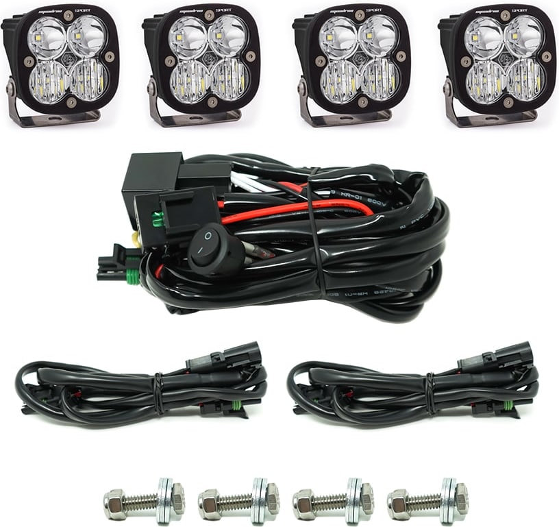 Grille Light Kits by Baja Designs: Four Squadron Sport pods with clear lenses, a switch harness, two extension harnesses and four mounting bolts on white.