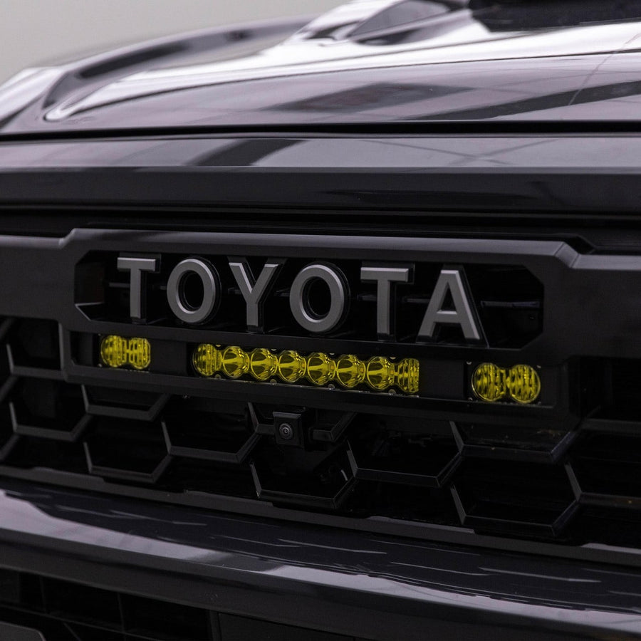 Grille Light Kits by Baja Designs: An amber 10 inch S8 bar between two amber S2 Pro pods sits under the TOYOTA lettering of a dark Tacoma grille.