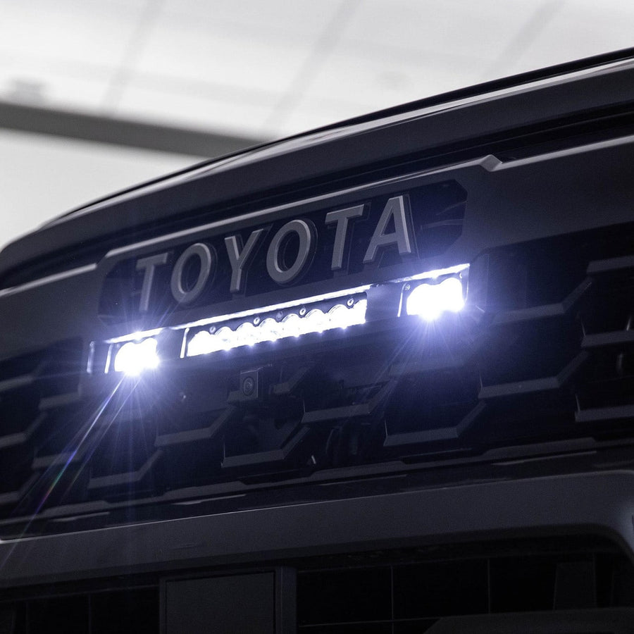 Grille Light Kits by Baja Designs: A 10 inch S8 bar and two S2 Pro pods shine bright white beneath the TOYOTA lettering of a dark Tacoma.