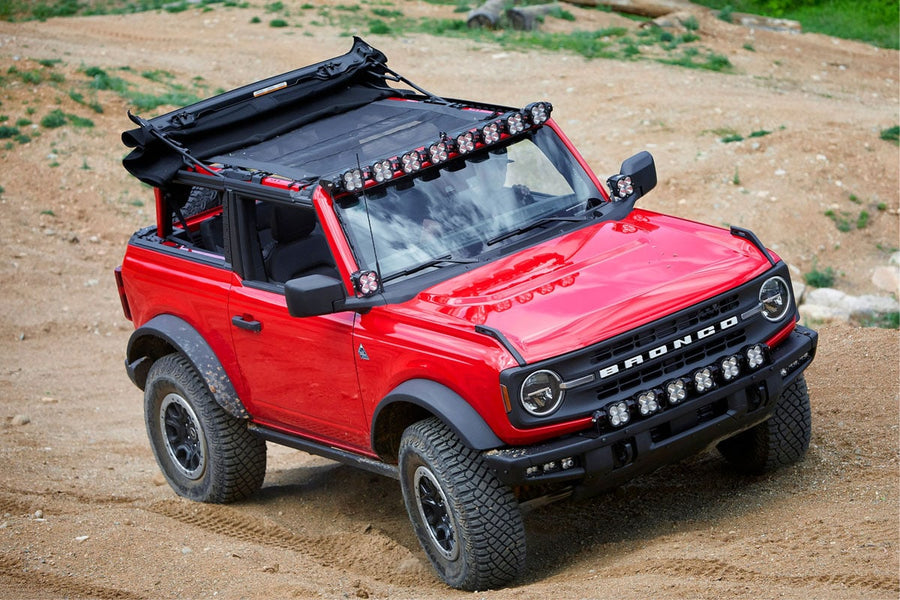 Roof Light Kits by Baja Designs: A red Ford Bronco with its soft top folded back carries a linkable LED pod roof bar above the windshield on a dirt trail.