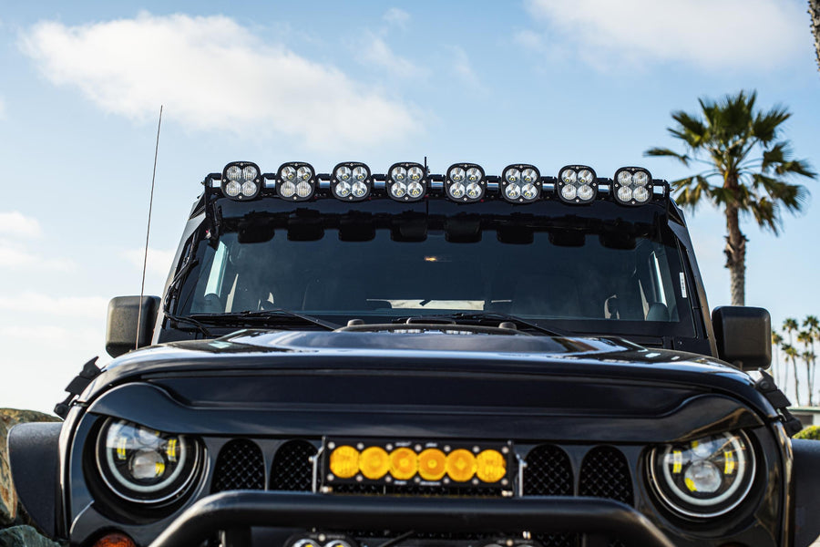 Roof Light Kits by Baja Designs: The front of a black Jeep shows a linkable LED pod bar above the windshield and an amber light bar in the grille.