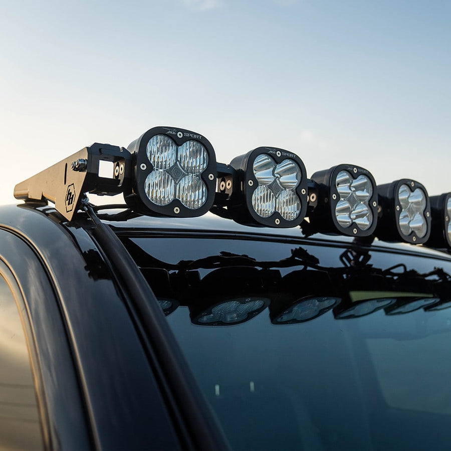 Roof Light Kits by Baja Designs: Large square LED pods on a linkable bar sit over the glossy roof of a dark vehicle against the sky.