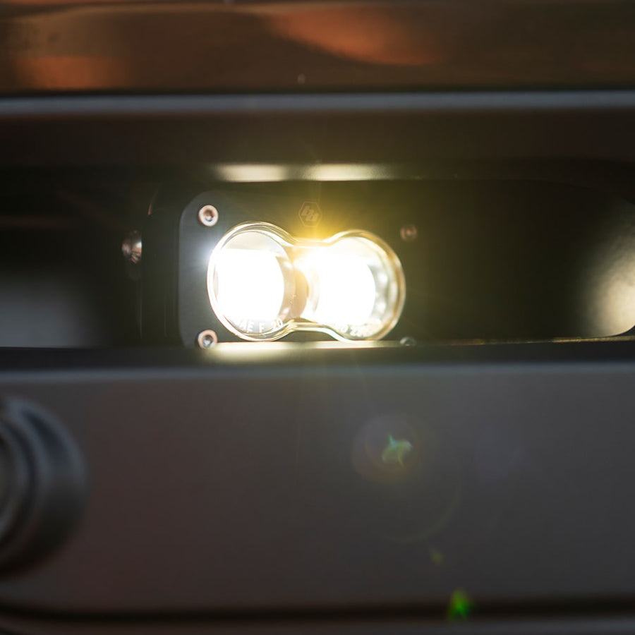 S2 Light Pods by Baja Designs: A lit S2 SAE pod with a clear lens glowing warm white inside a dark bumper opening.