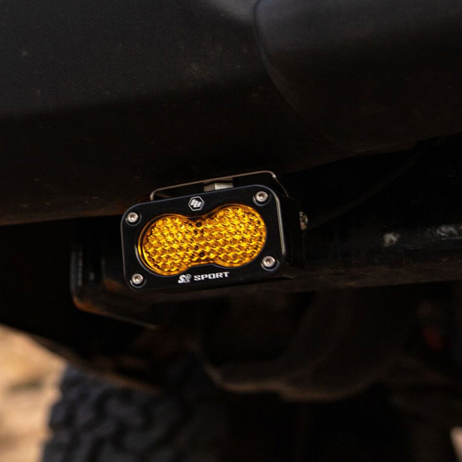 S2 Light Pods by Baja Designs: An S2 Sport pod with an amber honeycomb lens mounted low on the back of a dark vehicle near a tire.