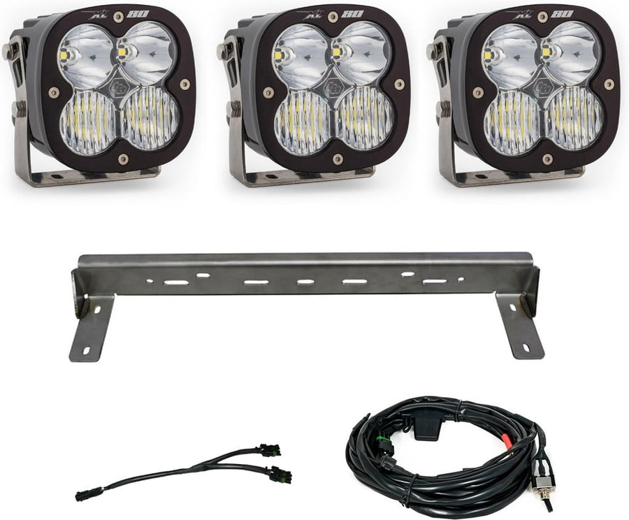 Bumper Light Kits by Baja Designs: Three XL80 LED pods with clear lenses, a steel bumper mounting bar and wiring harnesses on a white background.