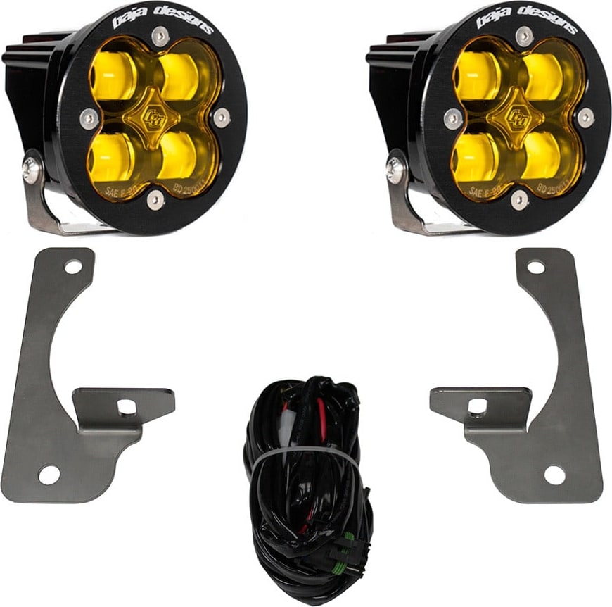 Fog Light Kits by Baja Designs: A pair of black Squadron-R pods with amber lenses shown with two fog pocket brackets and a wiring harness on white.
