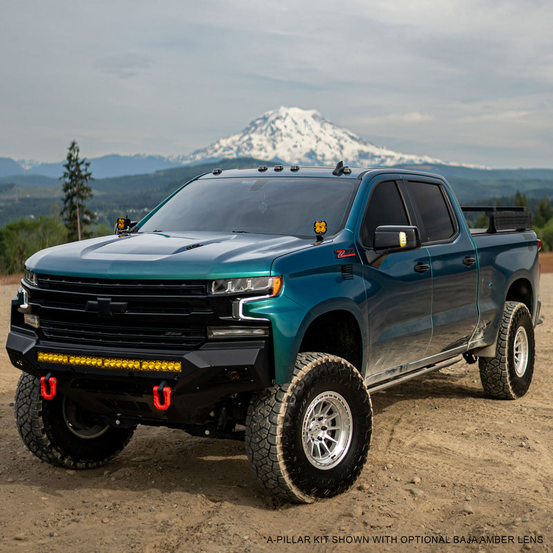 Baja Designs Squadron 2.0 Pro A-Pillar Light Kit installed on a Chevrolet Silverado 1500: A lifted teal Chevrolet Silverado with amber pods on both A-pillars, parked on dirt in front of a snowy mountain