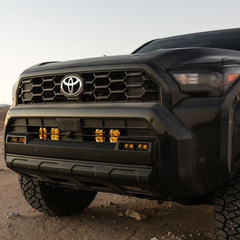 Baja Designs Squadron 2.0 Pro Behind-the-Grille Light Kit on a Toyota: close front view of a dark Toyota with lit amber pods behind the lower grille openings at dusk