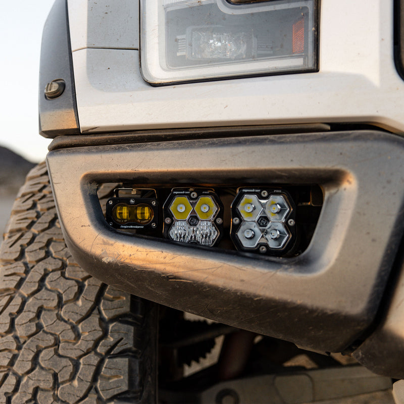 Baja Designs Squadron 2.0 Pro/S2 SAE Pro Fog Pocket Light Kit on a Ford F-150 Raptor: close view of an S2 pod and two square Squadron pods installed in the fog pocket of a white pickup bumper