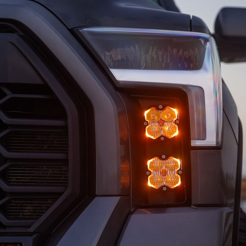 Baja Designs Squadron 2.0 Pro Vent Kit on a Toyota Tundra: two stacked Squadron pods glow amber in the vertical vent beside the headlight and grille of a dark gray truck
