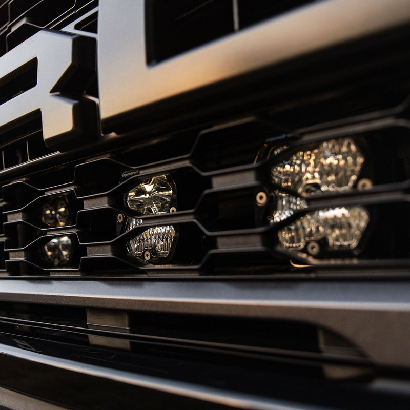 Baja Designs Squadron 2.0 Sport Behind-the-Grille Light Kit on a Ford F-150 Raptor: close angled view of clear Squadron pods mounted behind the slots of a Ford Raptor grille