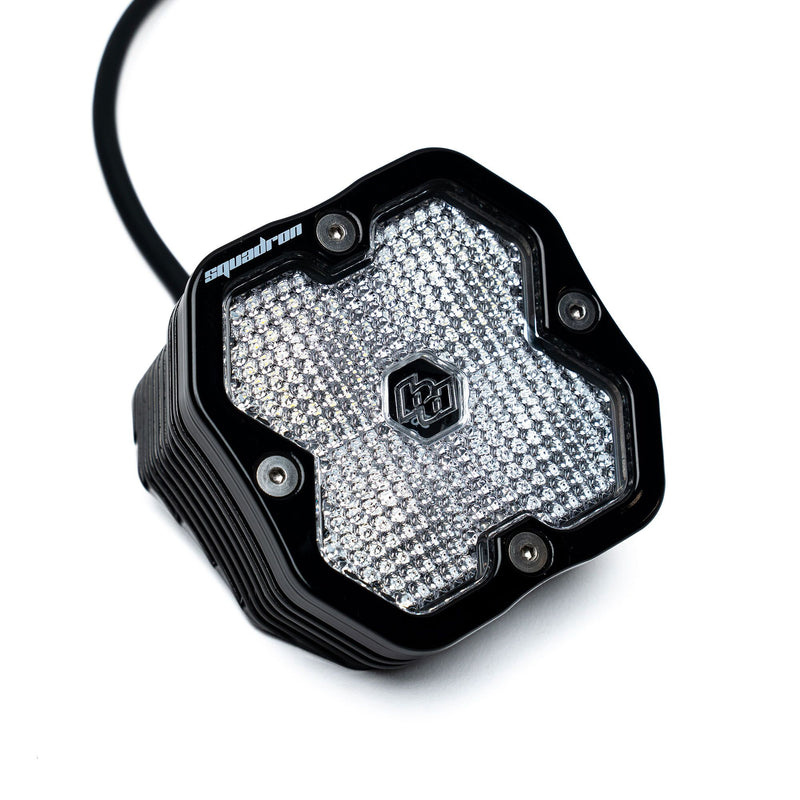 Baja Designs Squadron 2.0 Sport Black Angled Flush Mount LED Auxiliary Light Pod, whole product on a studio background: A black angled flush-mount Squadron LED pod with a clear diffused lens and wire pigtail on a white background