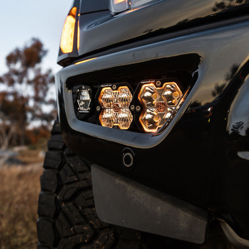 Baja Designs Squadron 2.0 Sport/S1 Fog Pocket Light Kit on a Ford F-150 Raptor: two square pods and a small pod glow in the lower bumper fog pocket of a black Ford pickup