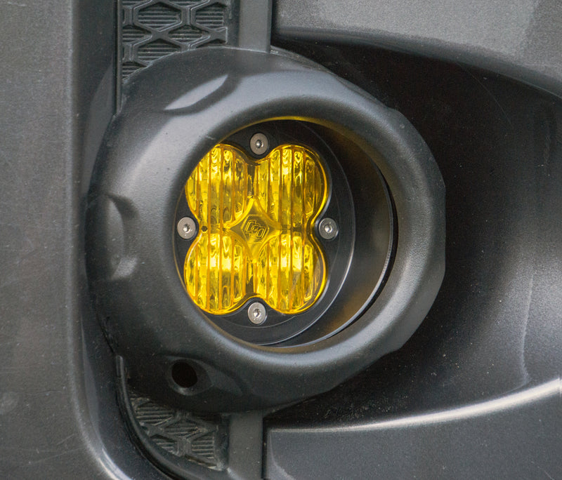 Baja Designs Squadron Angled Bezel on a vehicle: A Squadron pod with an amber lens sits in a round black bezel inside a gray bumper fog pocket; the bezel angle is hard to confirm from this view
