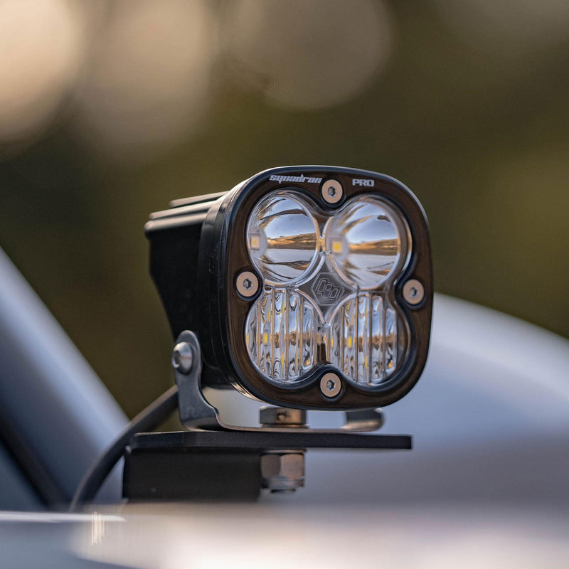 Baja Designs Squadron Pro A-Pillar Kit on a vehicle: A Squadron Pro pod on a black A-pillar bracket beside a windshield in soft evening light