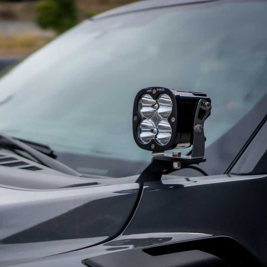 Baja Designs Squadron Pro A-Pillar Light Kit on a vehicle: A Baja Designs XL series (badge not legible) LED pod mounted on an A-pillar bracket beside the windshield of a dark gray truck