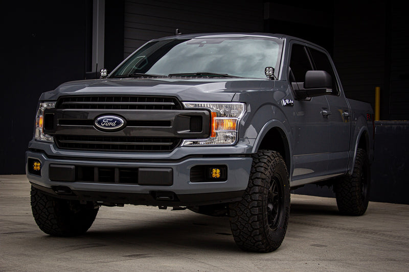 Baja Designs Squadron Pro A-Pillar Light Kit installed on a Ford F-150: A gray Ford F-150 parked in front of a dark building with Squadron pods at both A-pillars