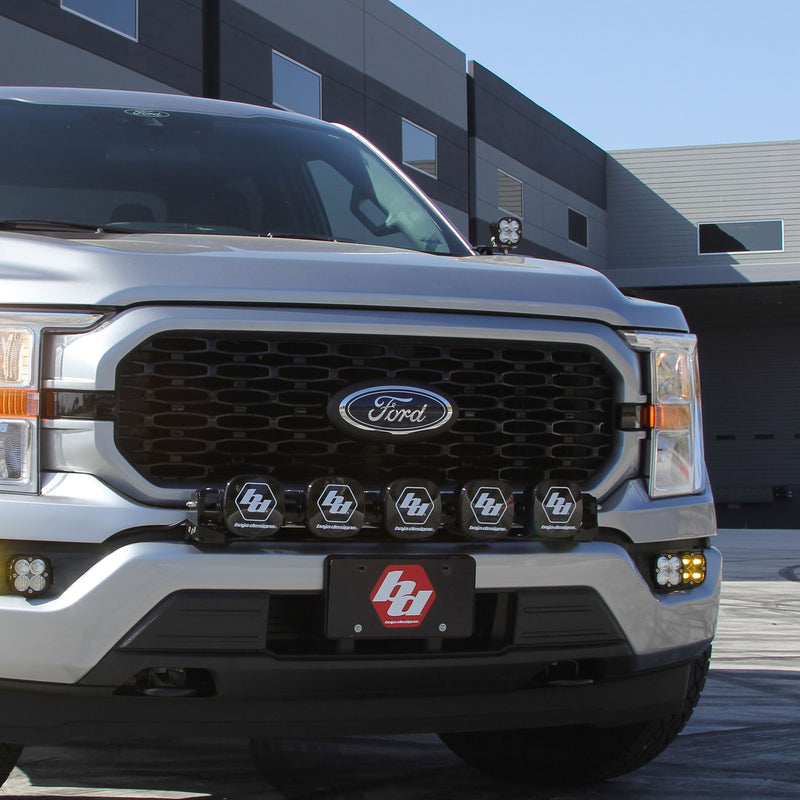 Baja Designs Squadron Pro A-Pillar Light Kit installed on a Ford F-150: A silver Ford F-150 front end with an A-pillar pod, a row of grille pods and amber fog lights