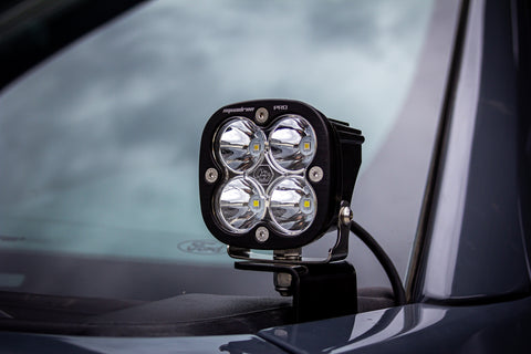 Baja Designs Squadron Pro A-Pillar Light Kit on a vehicle: A Squadron Pro LED pod with a clear lens mounted on an A-pillar bracket beside a gray windshield