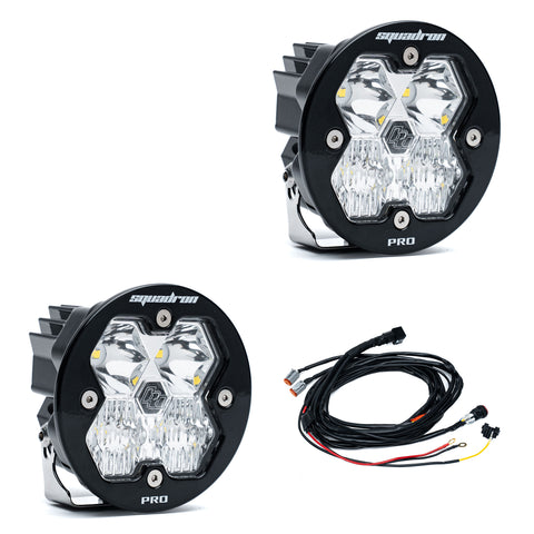 Baja Designs Squadron-R 2.0 Pro Black LED Auxiliary Light Pod Pair, whole product on a studio background: A pair of round black Squadron-R LED pods with clear diffused lenses and a wiring harness on a white background