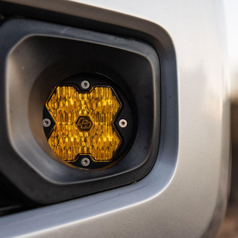 Baja Designs Squadron-R 2.0 Sport Fog Pocket Light Kit on a Toyota Tacoma: amber lens Baja Designs fog light installed in the fog pocket of a silver Toyota pickup bumper