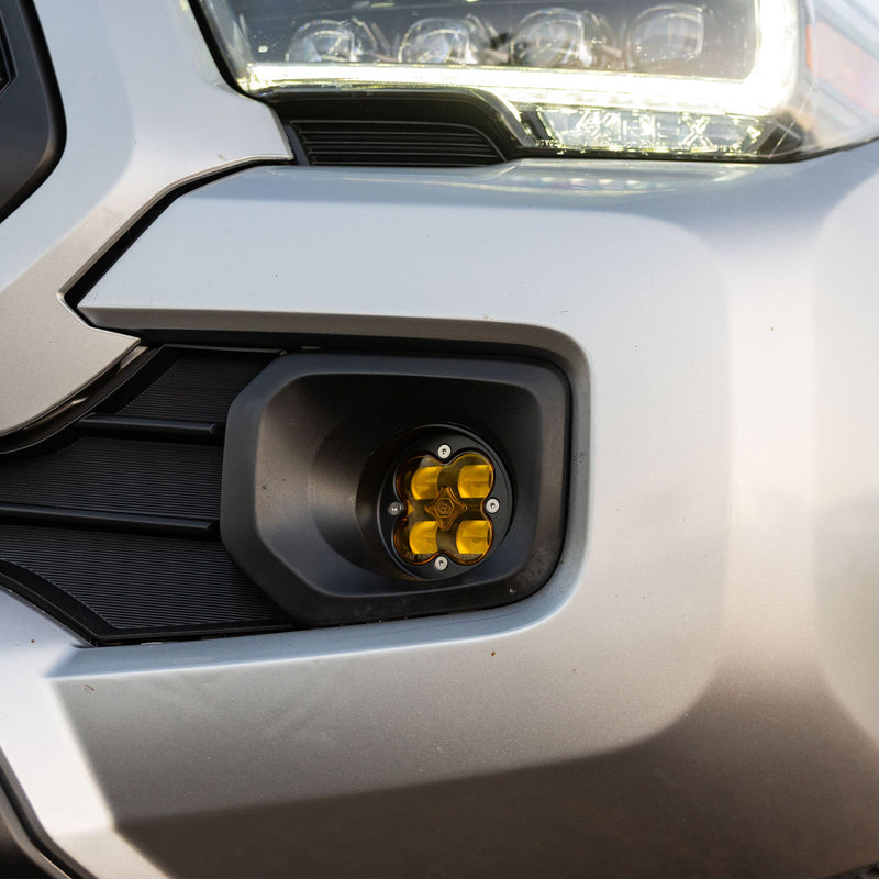 Baja Designs Squadron-R SAE Fog Pocket Light Kit on a Toyota Tacoma: silver Toyota Tacoma front corner with a round amber fog pod installed in the bumper fog pocket