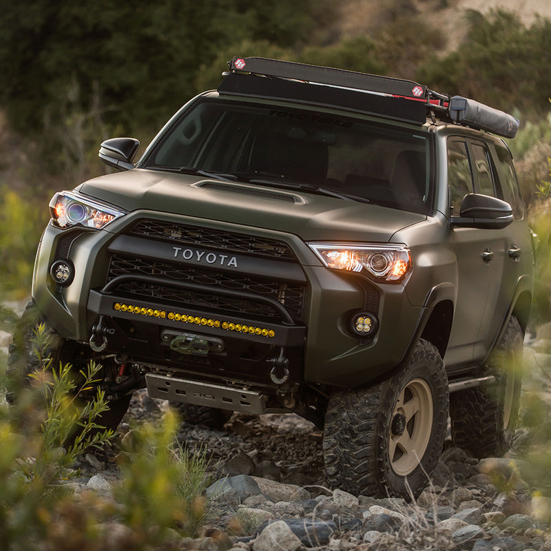 Baja Designs Squadron-R Sport Fog Pocket Light Kit installed on a Toyota 4Runner: A green Toyota 4Runner climbing a rocky trail with lit fog pocket lights and a lower bumper light bar
