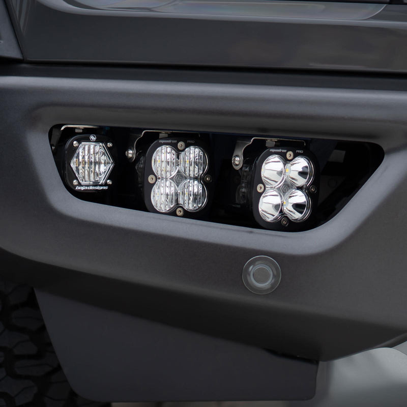 Baja Designs Squadron SAE/S1 Fog Pocket Light Kit on a vehicle: an S1 pod and two Squadron pods with clear lenses mounted in a dark gray truck bumper fog pocket
