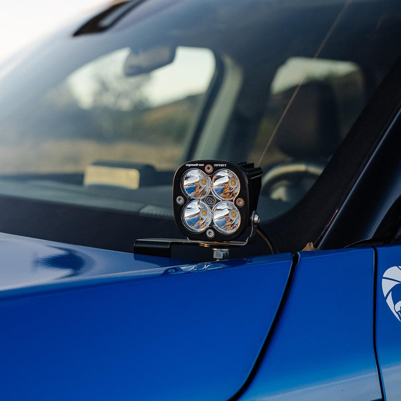 Baja Designs Squadron Sport A-Pillar Light Kit on a vehicle: A Squadron Sport LED pod with a clear lens on an A-pillar bracket beside the windshield of a blue vehicle