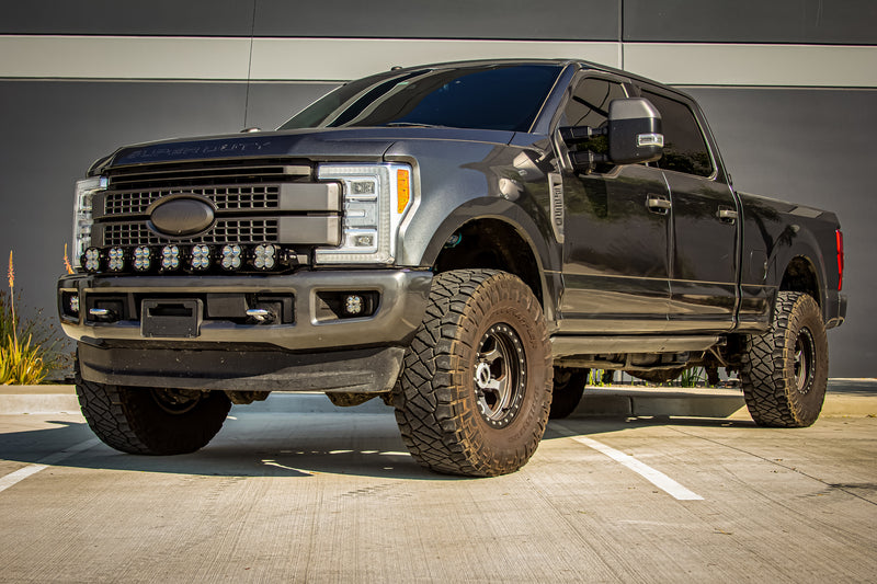 Baja Designs XL Linkable Bumper Light Kit installed on a Ford F-250 Super Duty: A lifted dark gray Ford Super Duty in a parking lot with a seven-pod XL Linkable light bar along the front bumper