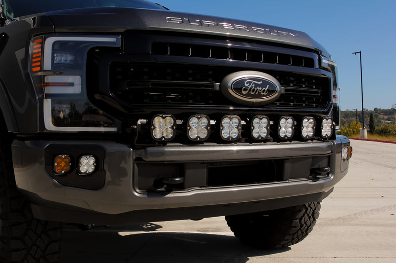 Baja Designs XL Linkable Bumper Light Kit on a Ford F-250 Super Duty: close front view of a gray Ford Super Duty with seven XL pods across the top of the front bumper and an amber fog pod