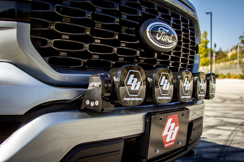 Baja Designs XL Linkable Bumper Light Kit on a Ford F-150: close view of a silver Ford F-150 grille with five XL pods wearing Baja logo covers and a Baja logo plate on the bumper