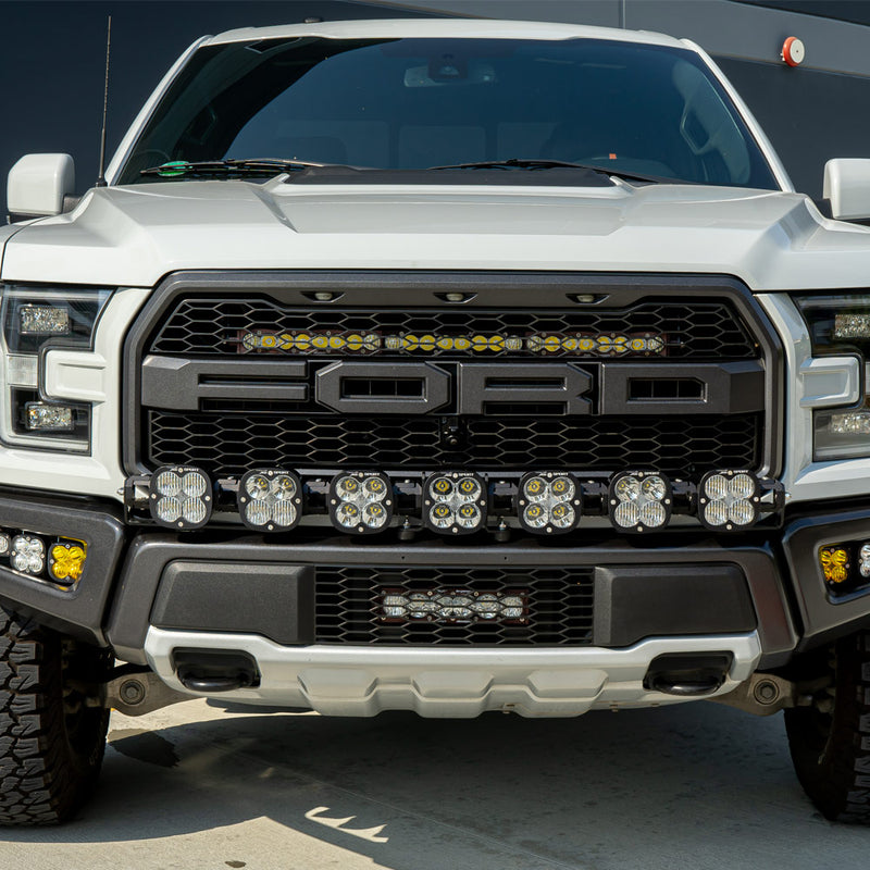 Baja Designs XL Linkable Bumper Light Kit installed on a Ford F-150 Raptor: front view of a white Ford Raptor with a row of XL pods across the lower grille, amber fog pods and a lit amber grille light bar