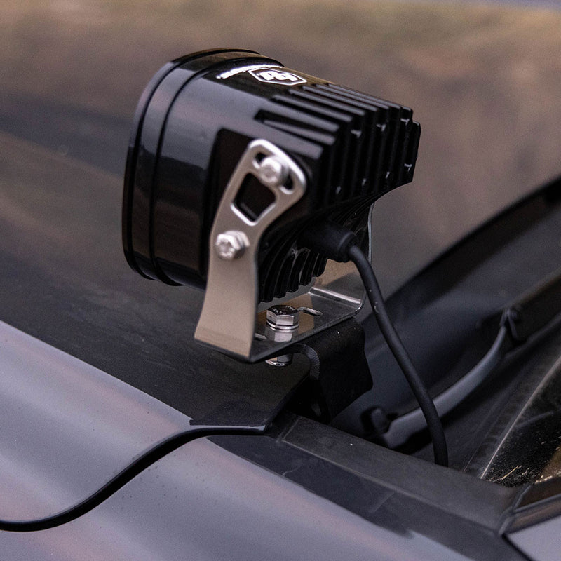 Baja Designs XL Pro A-Pillar Kit on a vehicle: the finned back of a Baja Designs XL LED pod on a silver bracket mounted at the A-pillar of a dark truck